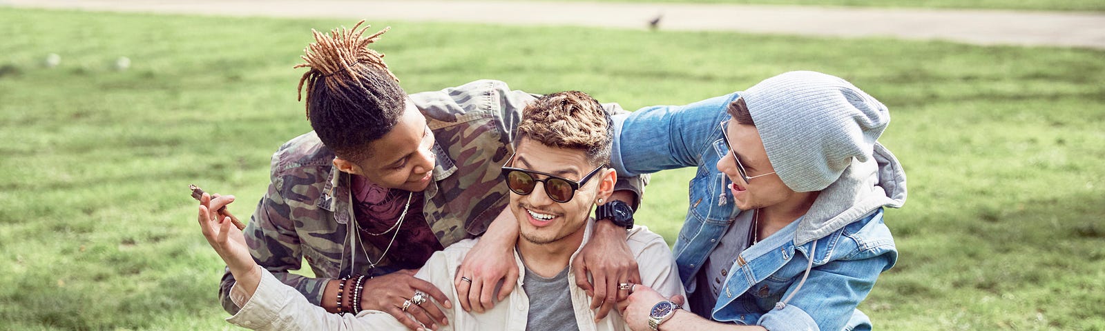 A teenage boy shrugs as his friends laugh in a circle around him at the park.