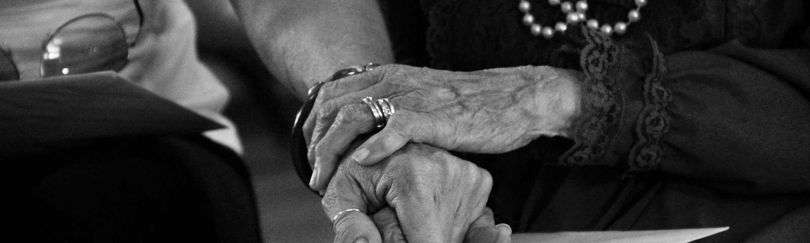 A black and white photograph of an elderly person resting her hand on a younger person’s arm in a gesture of loving support.