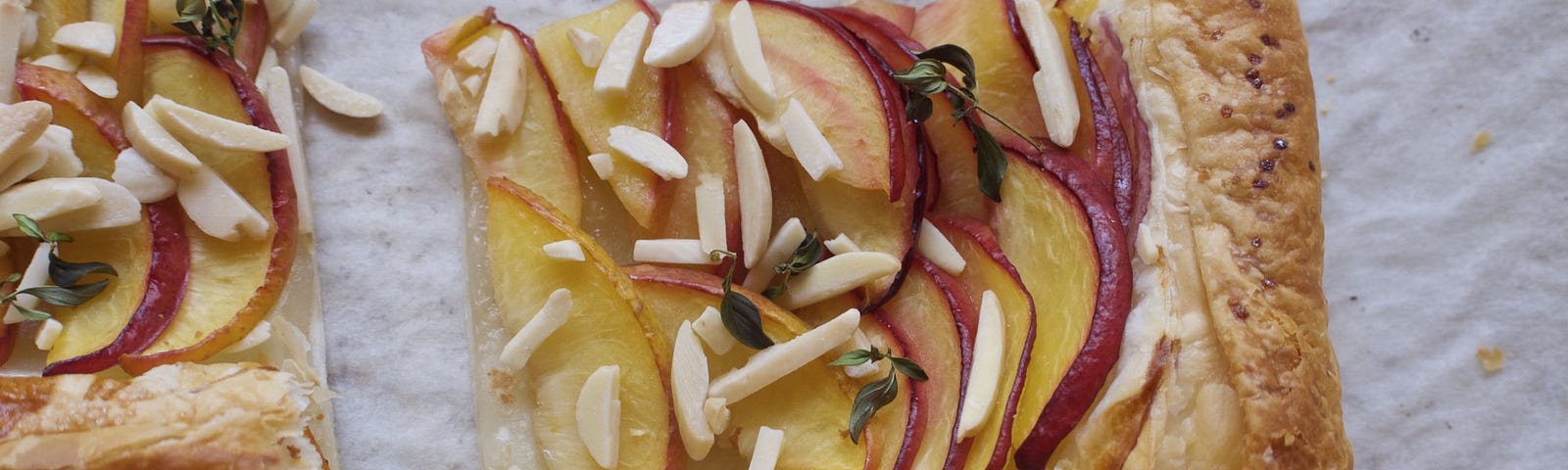 A tart topped with thinly-sliced peaches, sprinkled with slivered almonds.