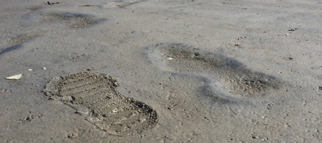 A crisp modern shoe print on sand, next to an eroded ancient footprint without any detail.