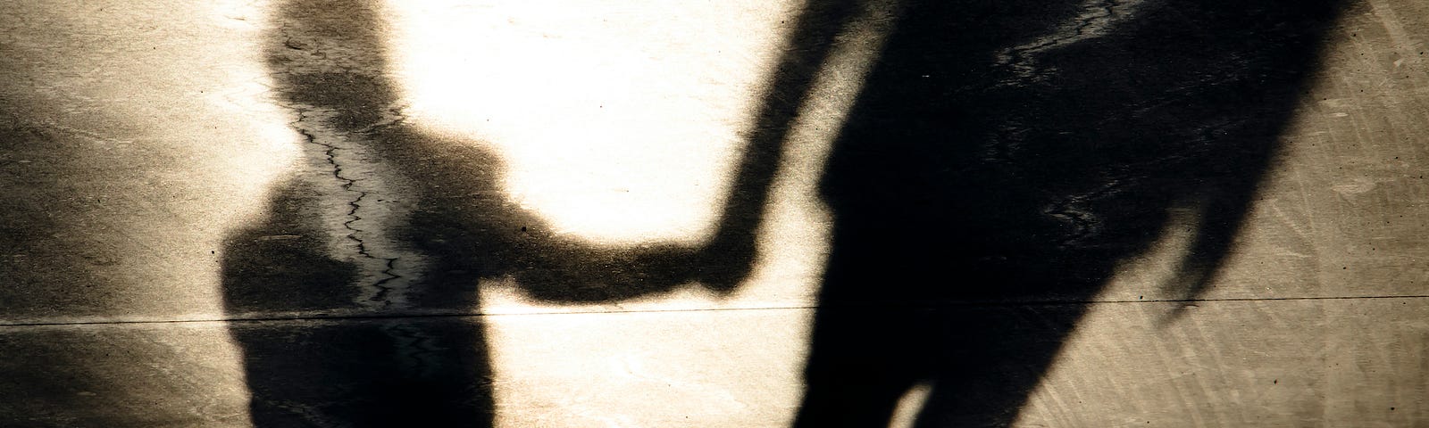 Shadows on pavement cast by a child and an adult holding hands as they walk.