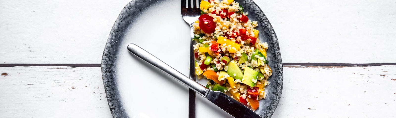 A fork and knife on a round plate in the position of clock hands, with salad in between as a symbol for intermittent fasting.