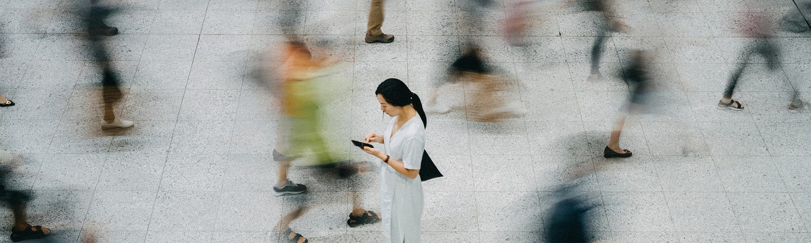 An overhead photo of an Asian woman standing still as blurred people walk by her.