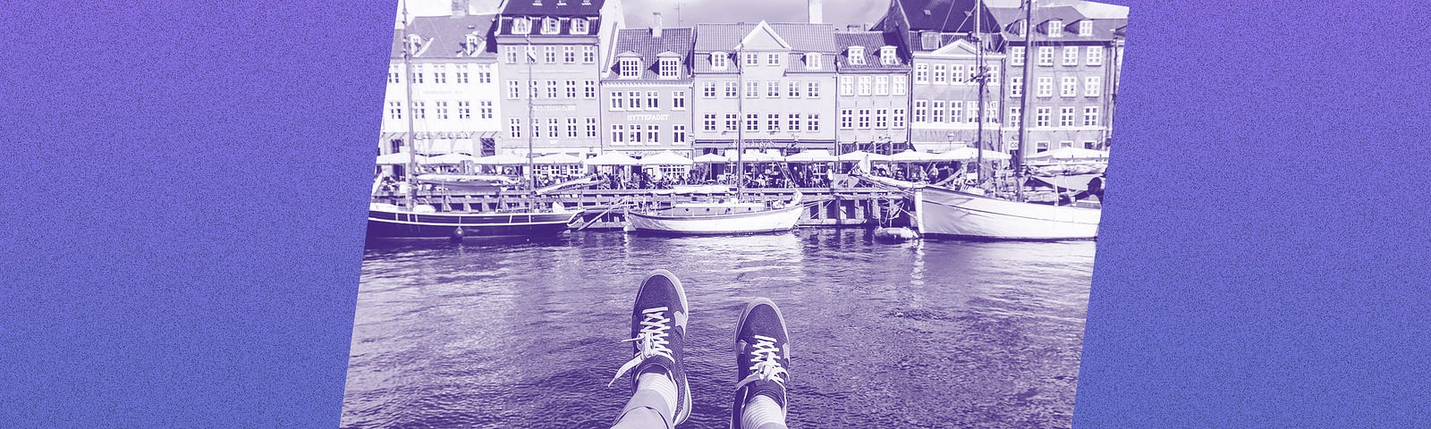 Filtered image of a person’s legs dangling over water with European buildings in the background.