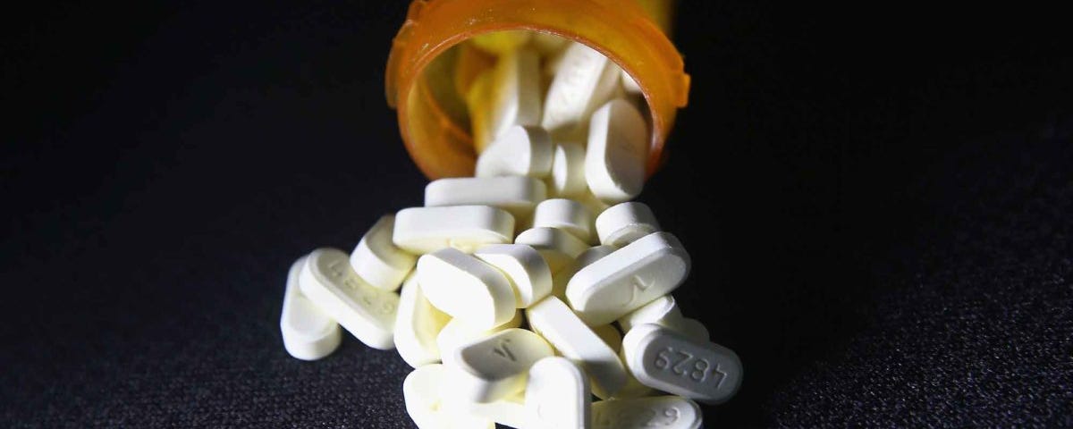 White elongated tablets spilling out of a translucent orange prescription bottle on a black background.