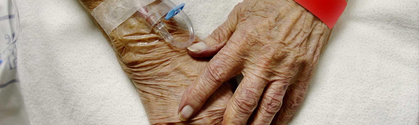 An elderly woman’s hands with IVs and hospital bracelets.