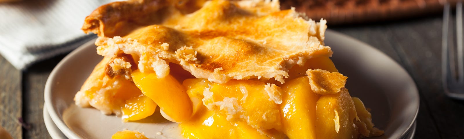 A slice of peach pie on a plate on a table made of dark wood.