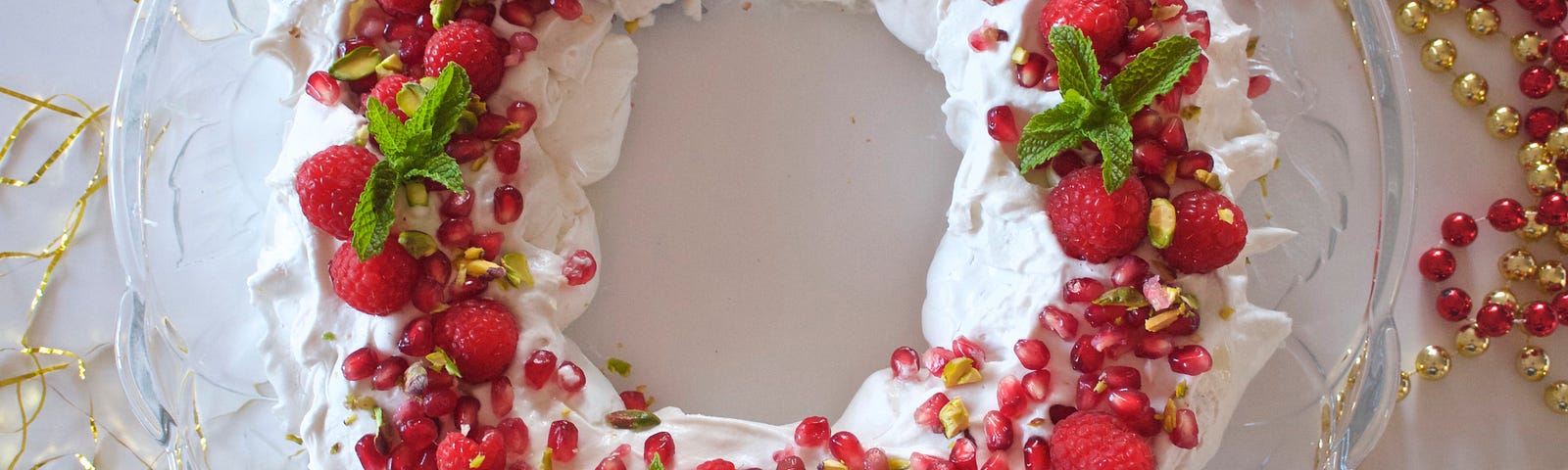 A wreath made of stiff sweet white vegan meringue sits on a plate and is decorated with red berries and leaves