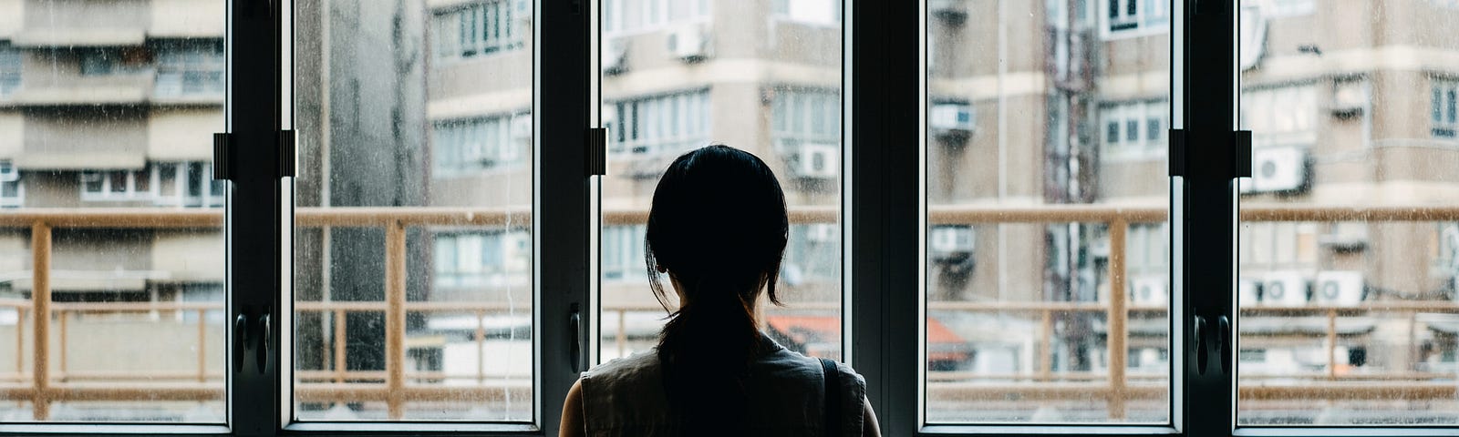 Rear view of woman looking out at the city through a window.