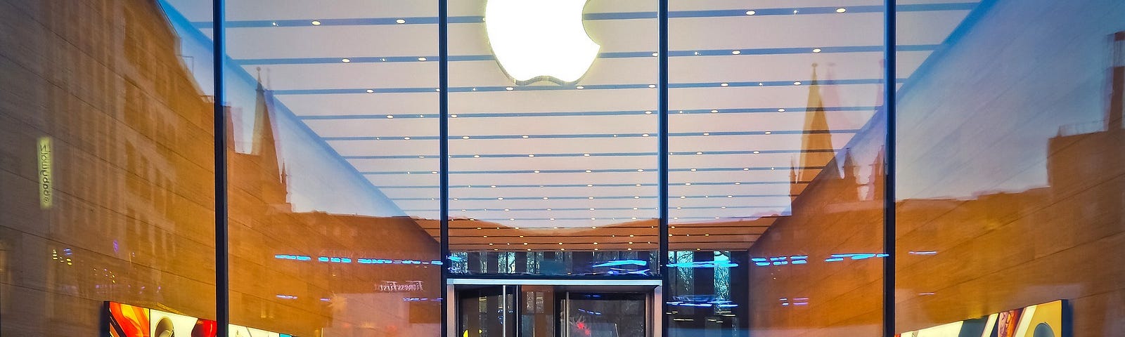 An Apple store with an all-glass front and a crowd of people milling about inside.