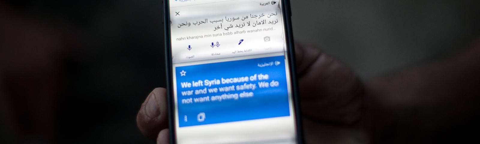 Photo of a man holding  his mobile phone that says “We left Syria because of war and we want safety” on Google Translate.