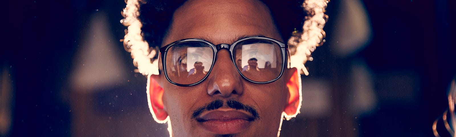 A photo of a mixed-race man, with a presentation reflected on his glasses.