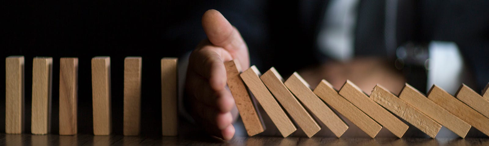 A hand in between a row of falling dominoes to stop them from knocking over the rest.