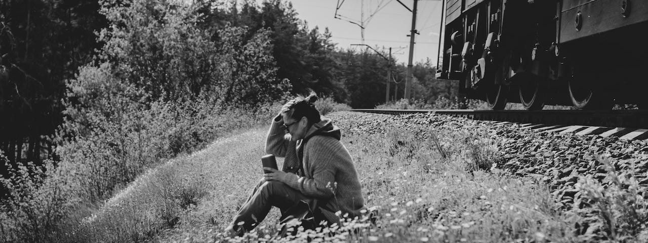 black and white image of woman sitting next to railroad tracks with her head in her hands