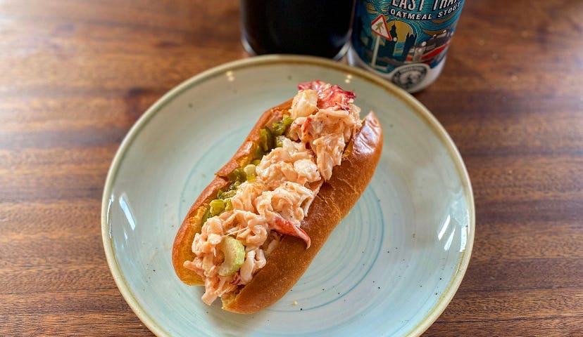 Photo of a lobster roll on a plate with a cup of beer next to it.