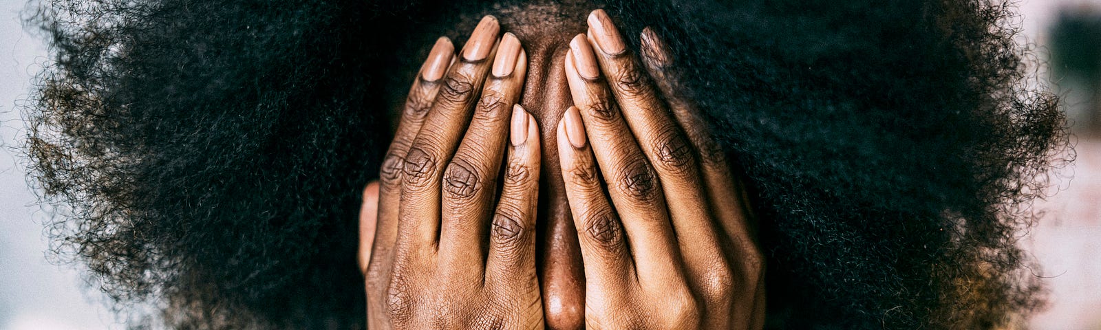 A photo of a black woman covering her face with her hands.