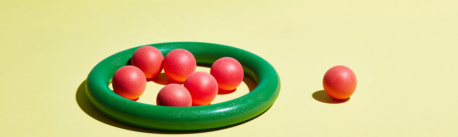 A single red sphere sits outside a group of red spheres contained within a green hoop.