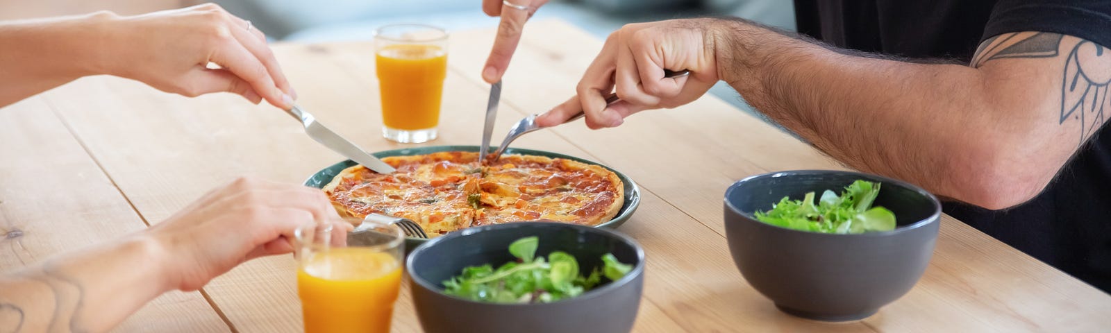 A man cutting a thin crust pizza, with orange juice, and a salad it’s a healthy meal.