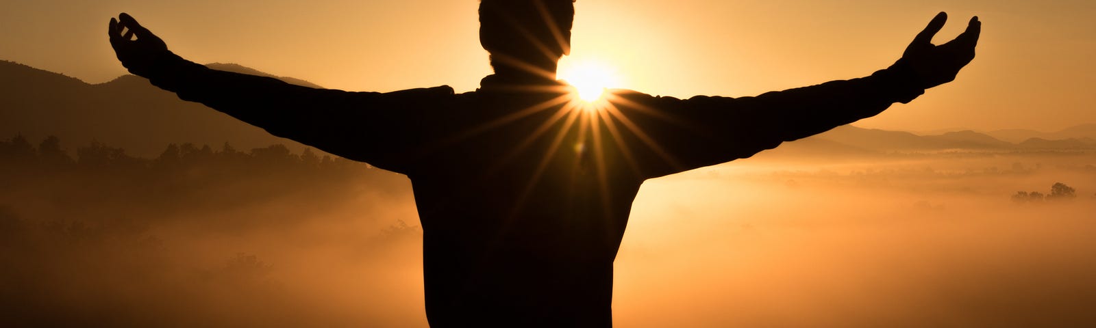 A silhouette of a man with outstretched arms looking at sunset.