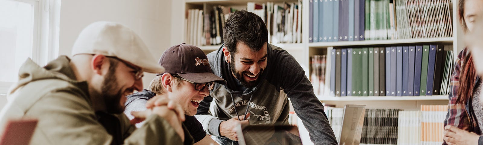 A group of smiling people crowded around a laptop depicting a happy and productive office environment.