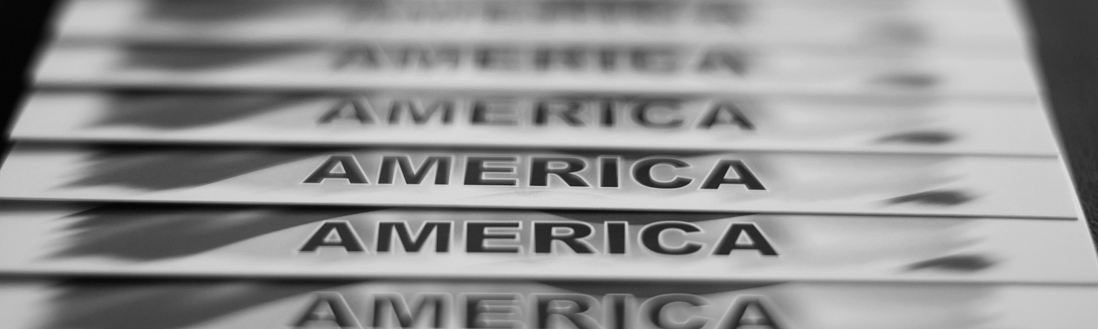 Black and white photo of a row of letter-sized papers with “America” printed at the bottom of each and displayed from foreground to background.