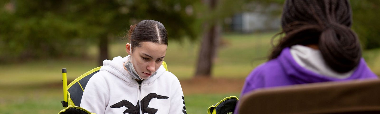 Two female high school students sit in lawn chairs outside, working on laptops.