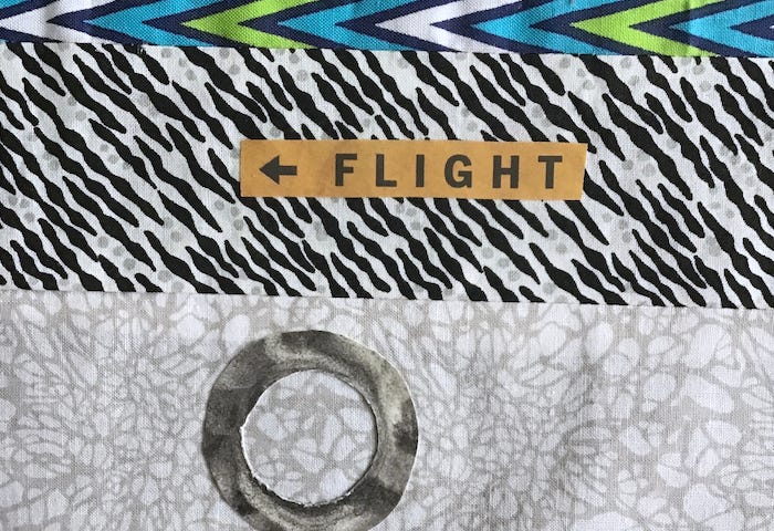 Detail of a fabric collage with the word Flight on top of a patterned fabric