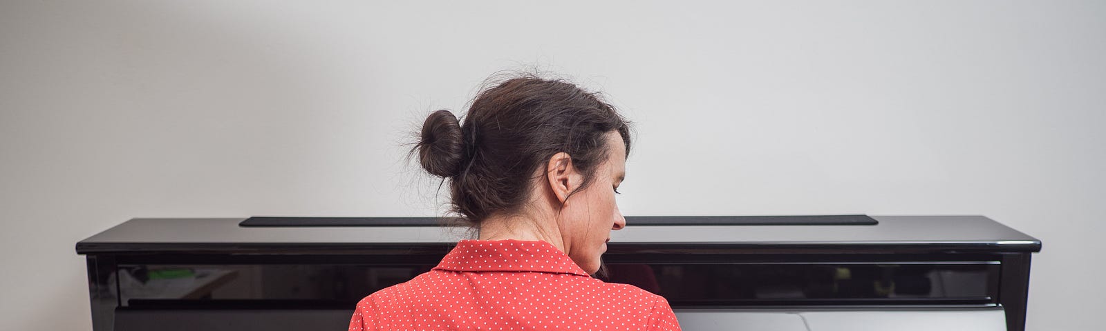 Rear view of a woman in a red dress playing the piano.