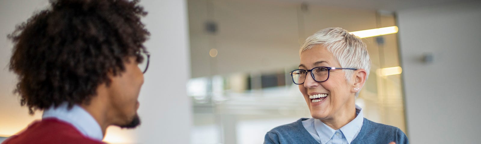 An older gray haired woman and younger  colleague shake hands during a meeting at the office.