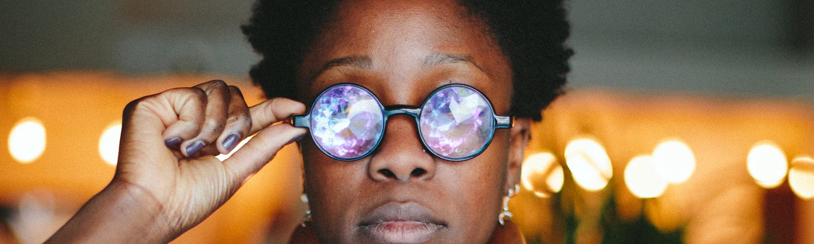 Yewande Komolafe wearing round glasses with iridescent lenses, holding a blurry dessert item.