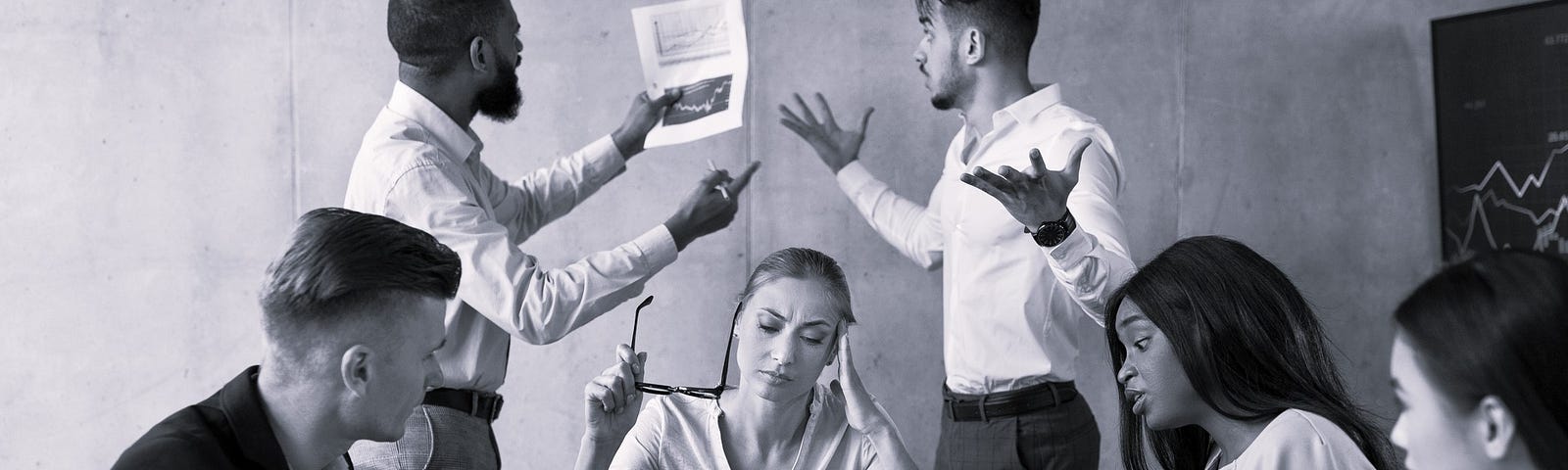 A group of multi-gender; multi-racial people is business attire sitting and standing around a conference table having a very animated dicussion.