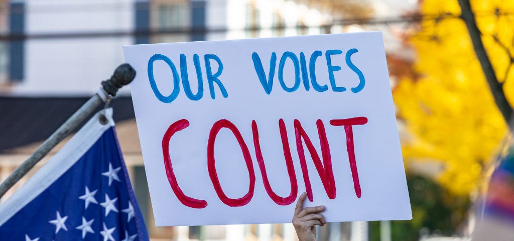 Protestor holding a sign that says “OUR VOICES COUNT.”