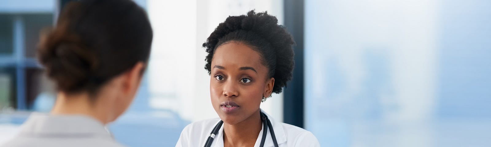 A cropped shot of a doctor, who is a woman of color, talking to a patient in her office.