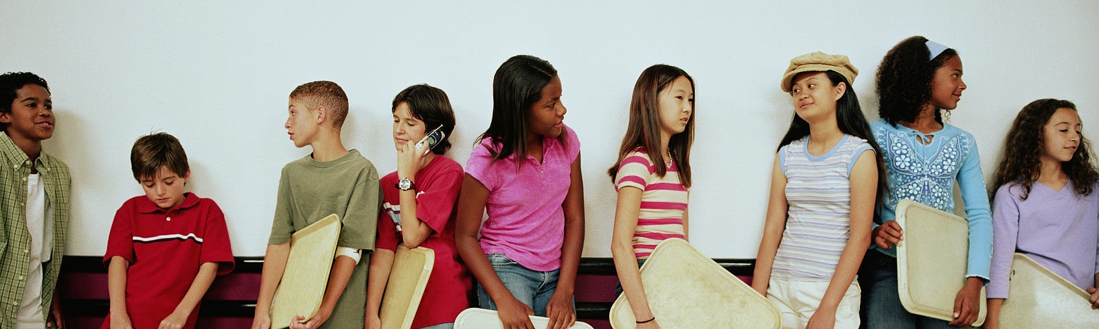 Middle school kids holding their trays wait in a school lunch line.