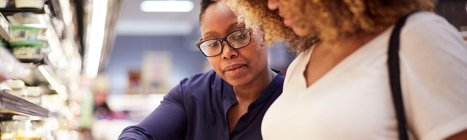 A photo of two black women examining food at the grocery store.