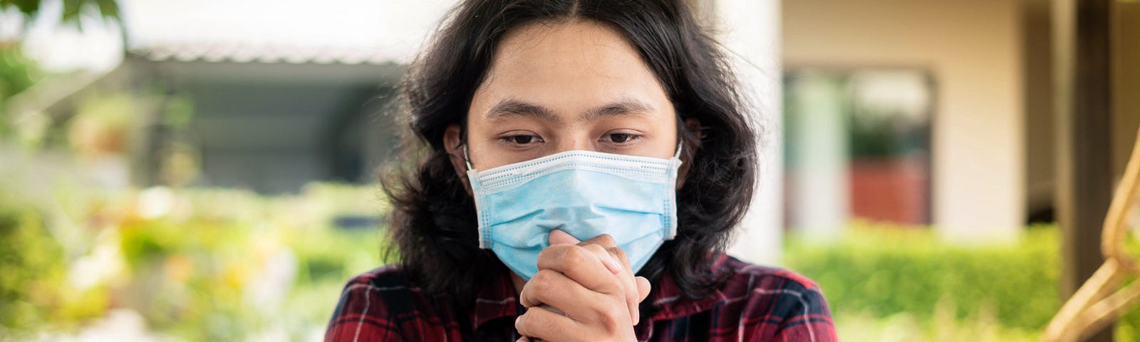 A man wearing a mask while sitting with his hands clasped.