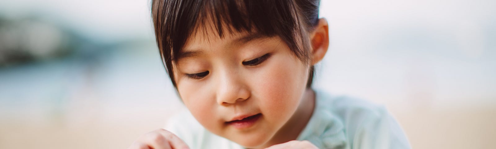 A  young girl chooses and picks a seashell from her father’s hand.