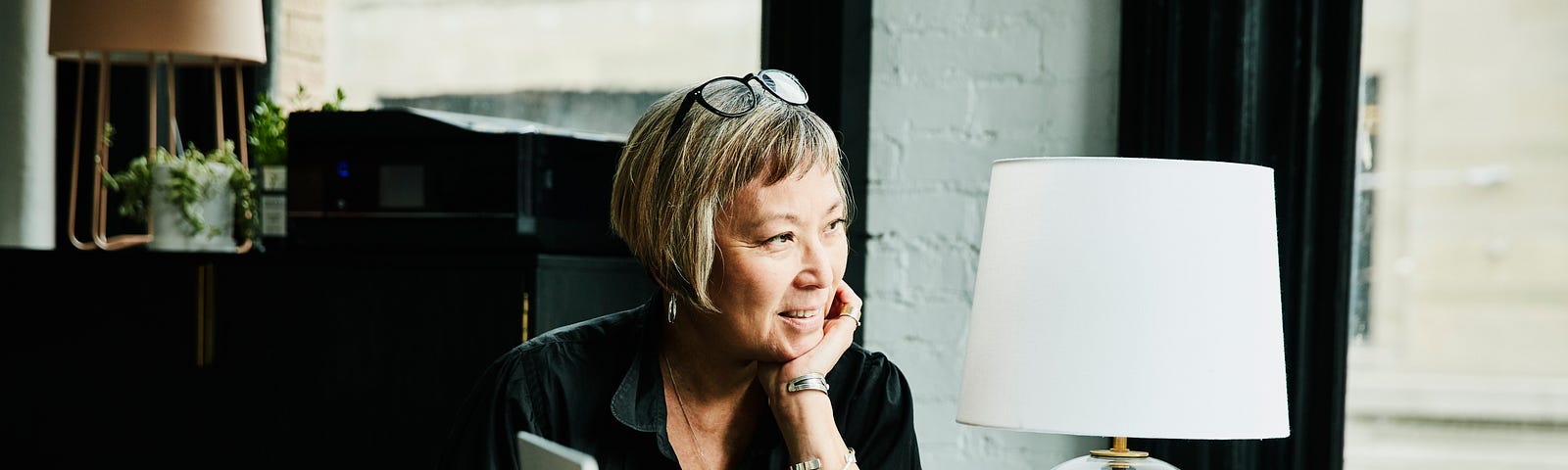 Older woman looking out window with her iPad in front of her on desk.