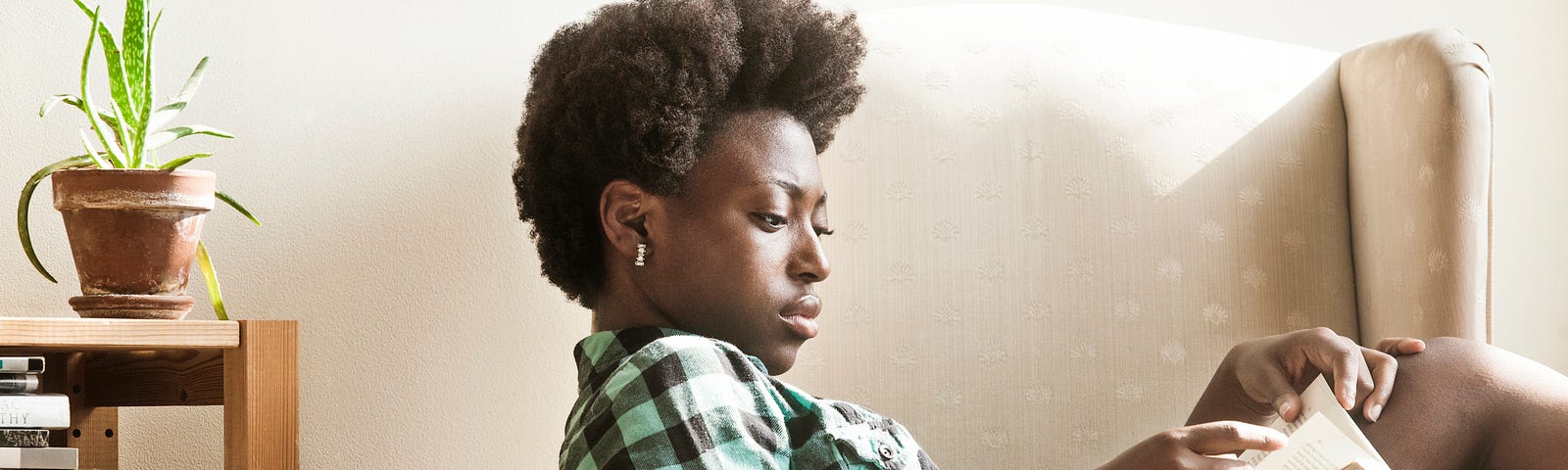 A photo of a black woman sitting in an armchair reading a book.