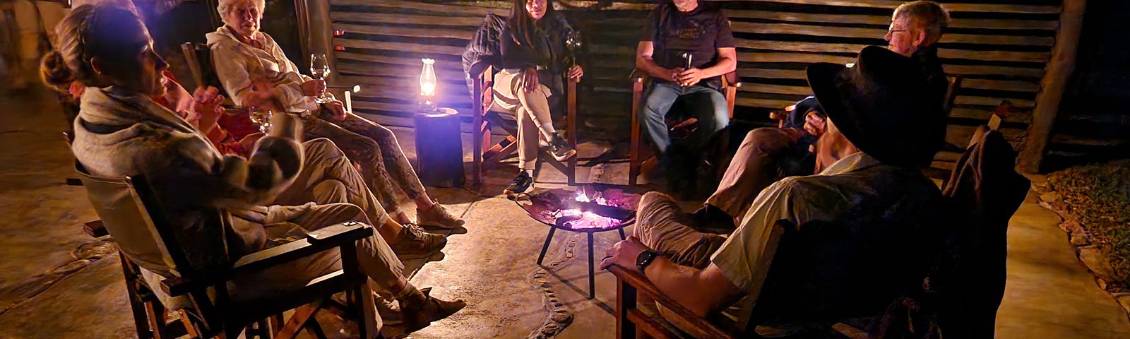 A group of people sitting on deck chairs around a campfire and a lantern