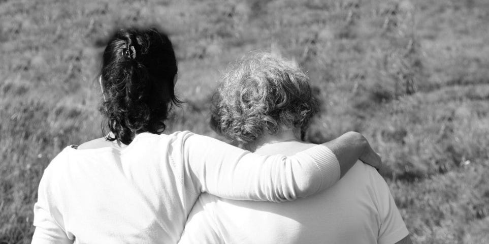 A rear shot of a mother and daughter walking with their arms around each other.