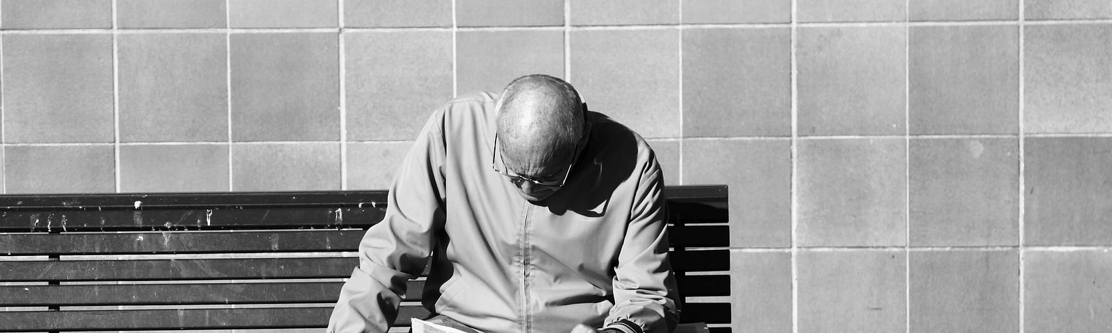 older man sitting on a bench, reading a newspaper