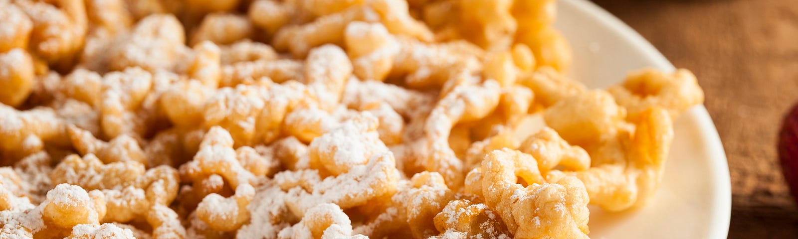 A plate of a powdered sugar-dusted funnel cake, on a red-and-white gingham cloth.