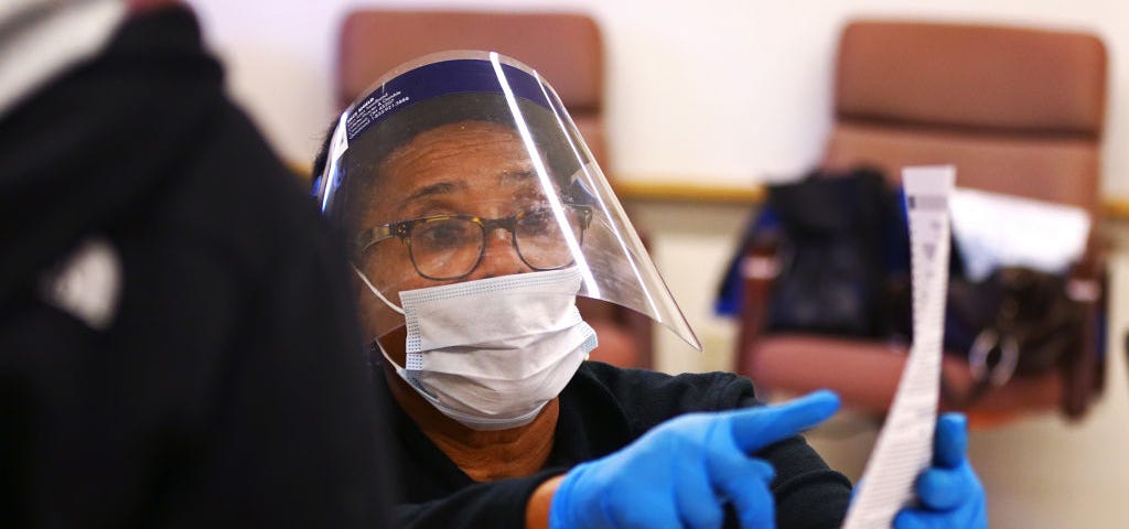 Poll worker wearing face mask and face shield helping a voter at the polls.