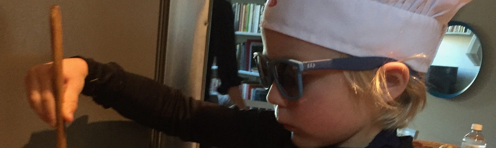 A kid with a chef’s hat, stirring something in a pot.