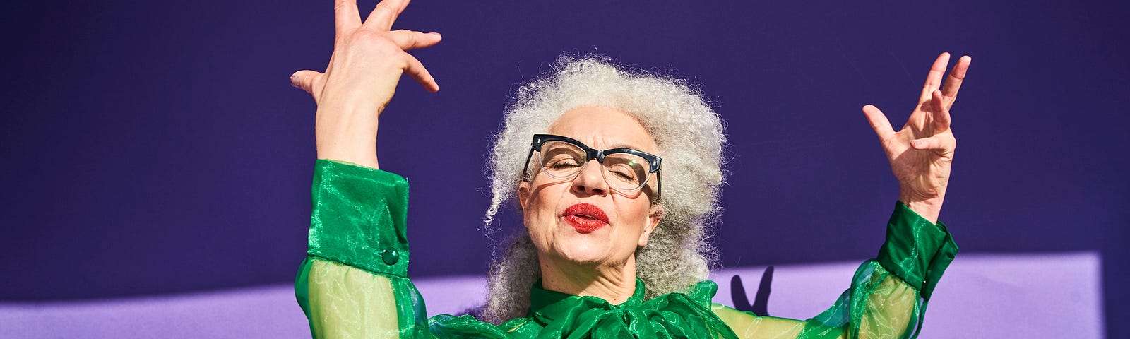 Confident senior woman in green against a violet background throwing up a confident pose.