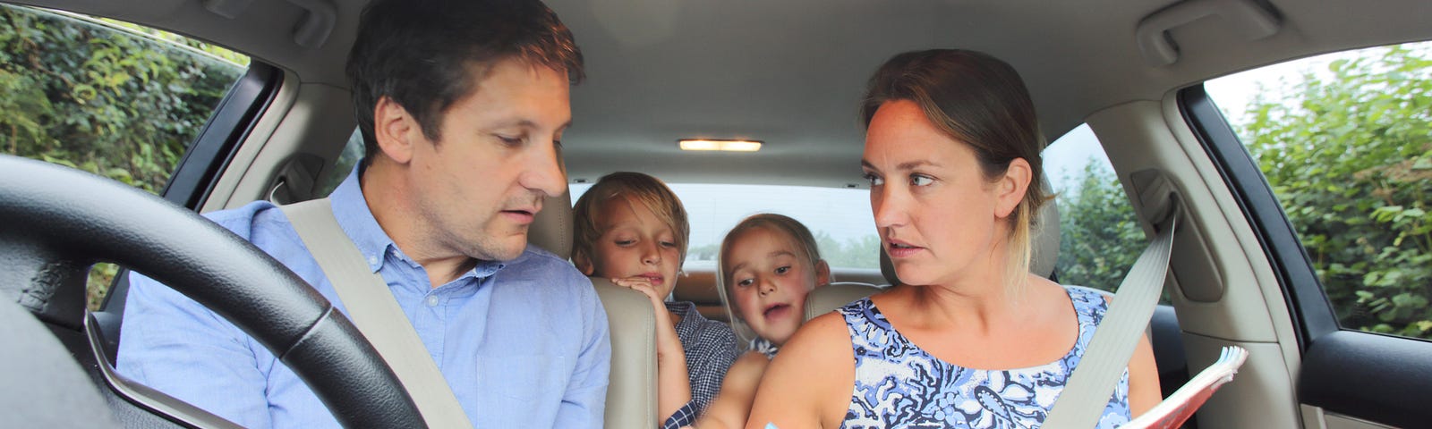 2 parents fight over map directions in the car while their children peer over the back seat.