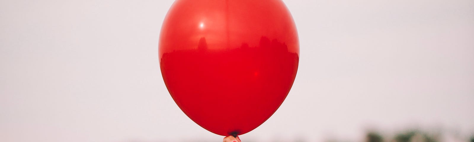 A red balloon in someone’s hand rising above greenery