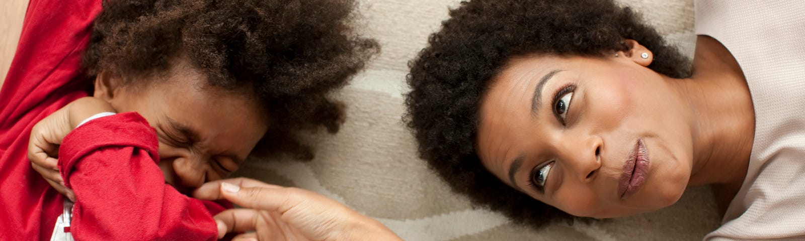 Black woman tickling a young Black boy, he is giggling and covering his face.