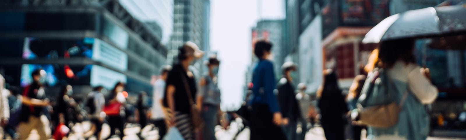 Blurred image of people walking at a crosswalk in a city.